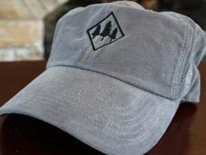 grey corduroy hat with tree design and back text saying "by the shores"